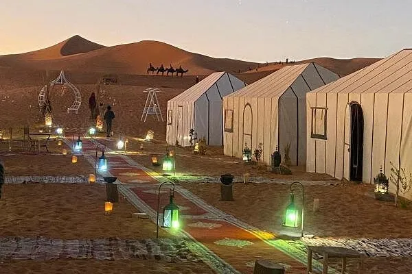 Tentes du campement à la tombée du jour, allée de tapis et lanternes dans les dunes