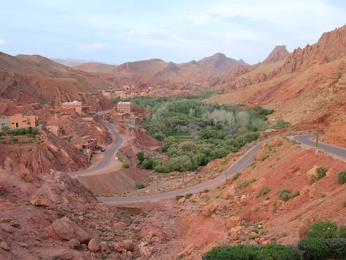 Route sinueuse dans une vallée de l’Atlas, entre roches rouges et palmeraie