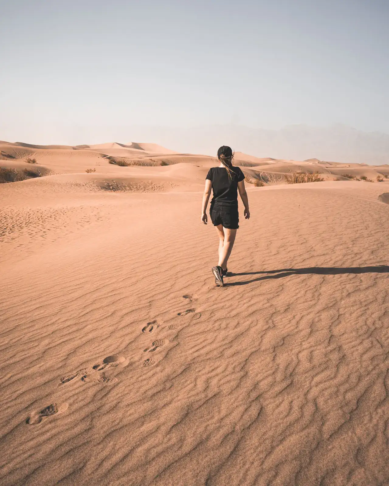 Une voyageuse marche seule dans les dunes, ses pas derrière elle